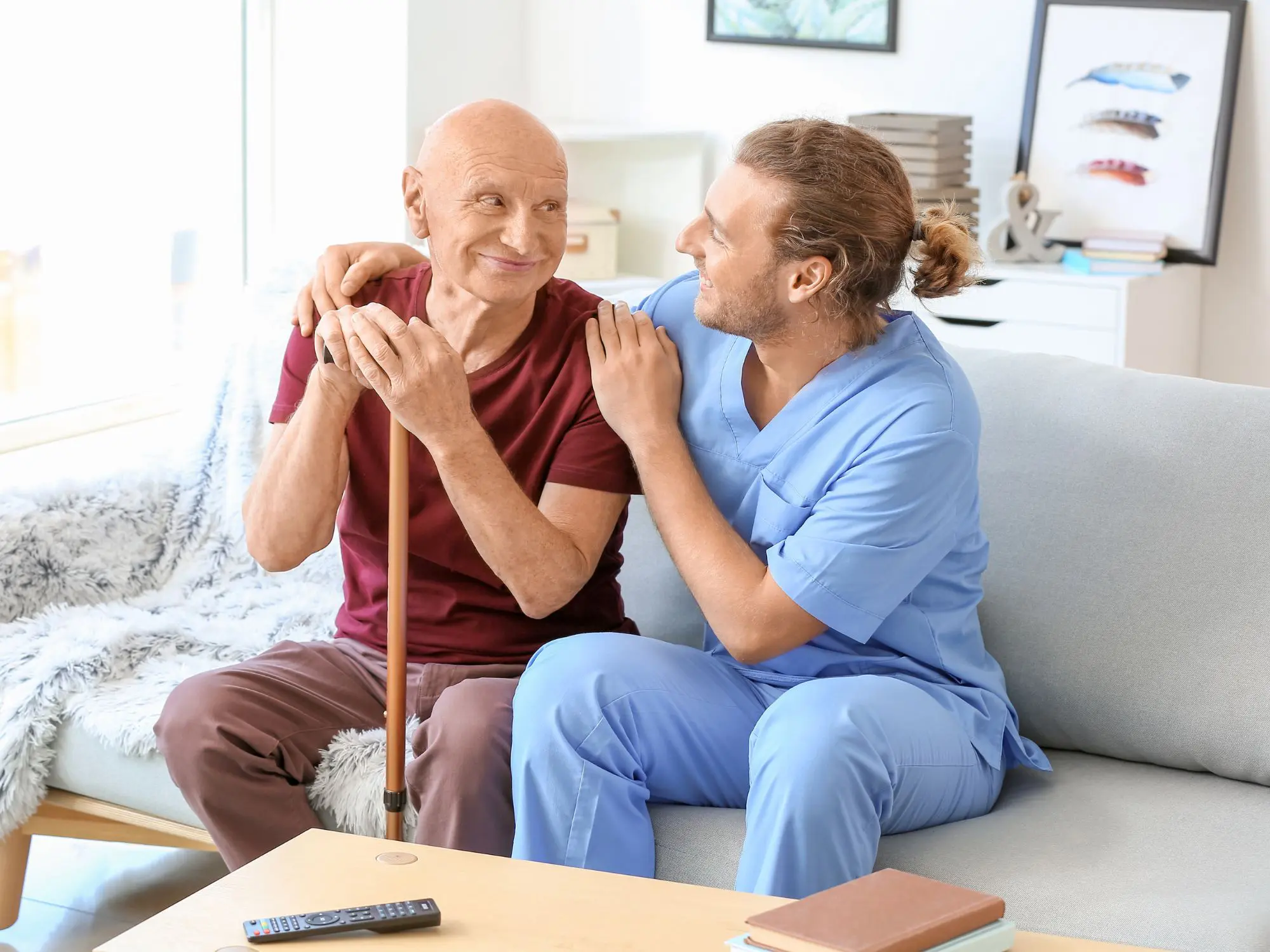 Elderly man with caregiver sitting on couch.