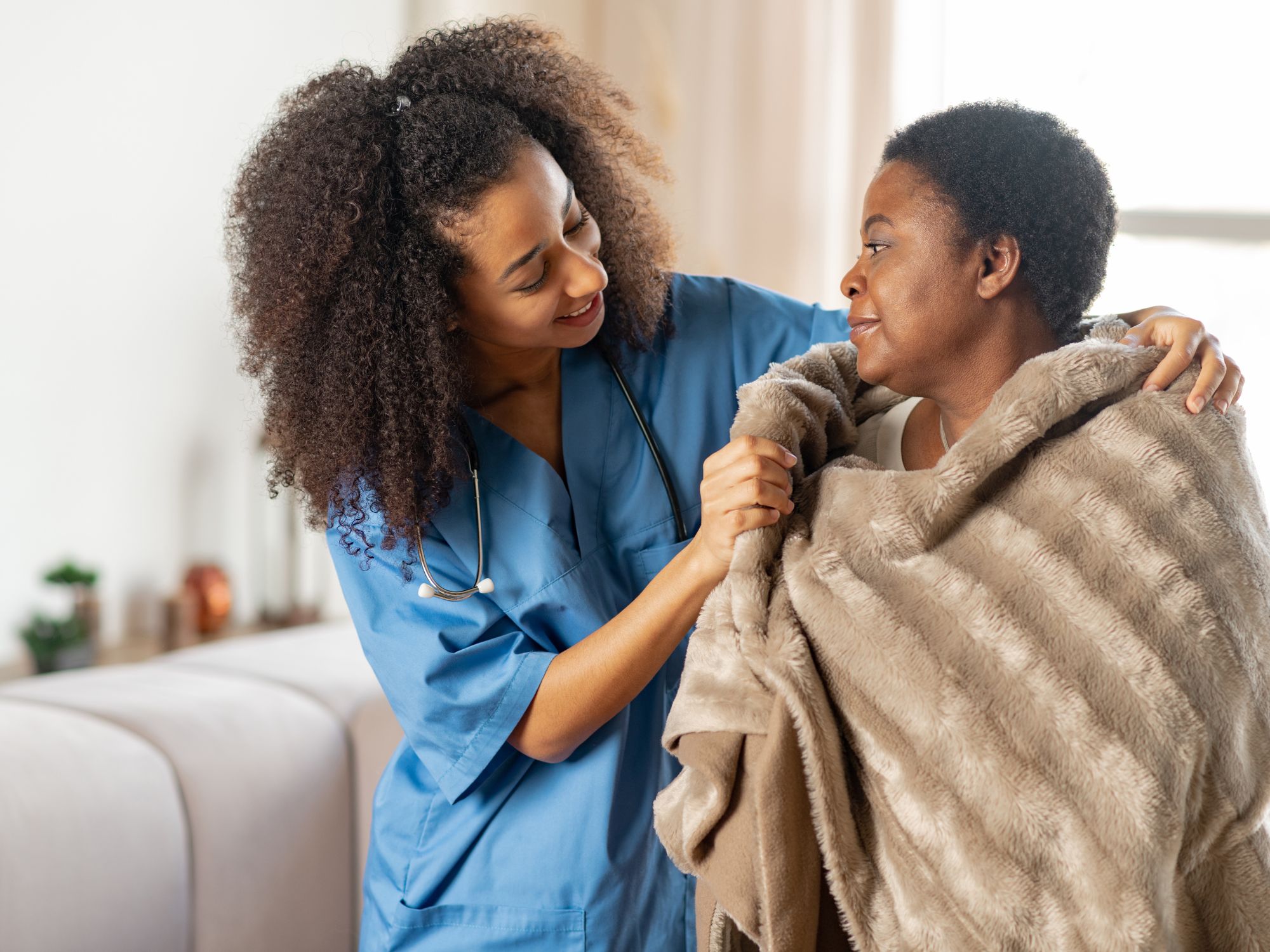 Nurse comforting elderly woman with blanket.